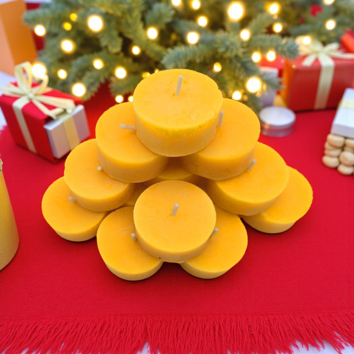 Eine pyramidale Anordnung aus runden, gelben Bienenwachskerzen auf einer roten Tischdecke, umgeben von weihnachtlichen Geschenken und einer Tannenbaum-Lichterkette.