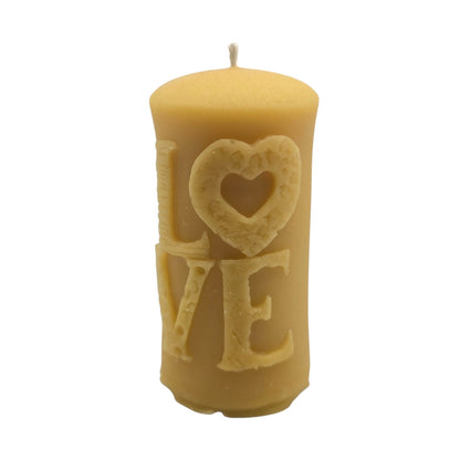 Eine zylindrische Stumpenkerze aus naturfarbenem, hellem Bienenwachs mit dem reliefartigen Schriftzug „LOVE“ auf der Vorderseite, bei dem das „O“ als Herz mit feiner Wabenstruktur gestaltet ist, sowie einem Docht oben