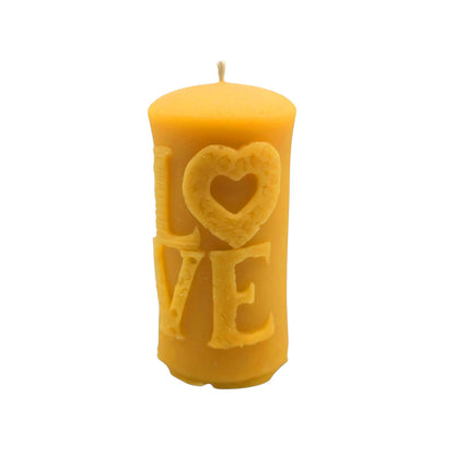 Eine zylindrische Stumpenkerze aus gelbem Bienenwachs mit dem erhabenen, reliefartigen Schriftzug „LOVE“ auf der Vorderseite, bei dem das „O“ als Herz geformt ist, sowie einem Docht oben.