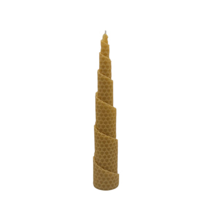 Eine handgefertigte Bienenwachskerze aus einer gerollten Wachsplatte in spiralförmiger Form, aufrecht stehend vor weißem Hintergrund.