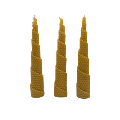 Ein Set aus drei handgefertigten Bienenwachskerzen, sorgfältig aus reinen Bienenwachs-Wachsplatten in eine spiralförmige Form gedreht, nebeneinander auf weißem Hintergrund.